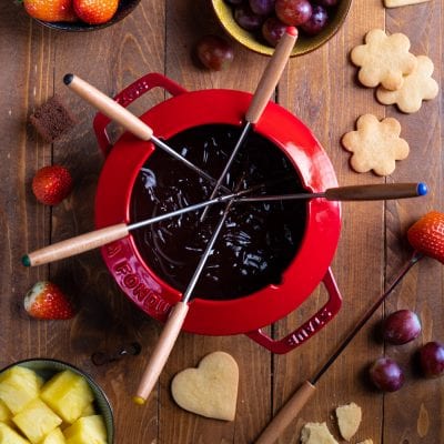 Fonduta di cioccolato con forchettine da fondue, fragole, uva, ananas e biscotti da intingere