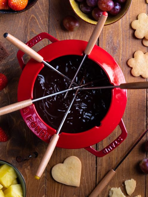 Fonduta di cioccolato con forchettine da fondue, fragole, uva, ananas e biscotti da intingere