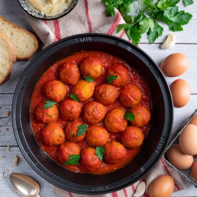 Pallotte cacio e ova in salsa di pomodoro, guarnite con foglie di prezzemolo fresco
