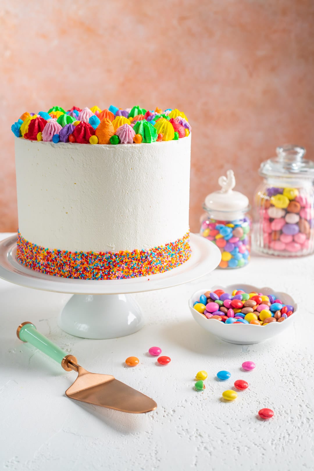 Torta sorpresa di compleanno decorata con ciuffetti di ganache colorata e codette sul bordo