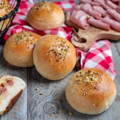 Bombe ripiene di provola e mortadella con granella di pistacchio in superficie, una tagliata a metà rivela il ripieno