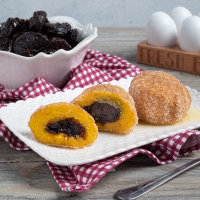Canederli dolci alle prugne impanati e fritti, uno tagliato a metà rivela il ripieno di prugna