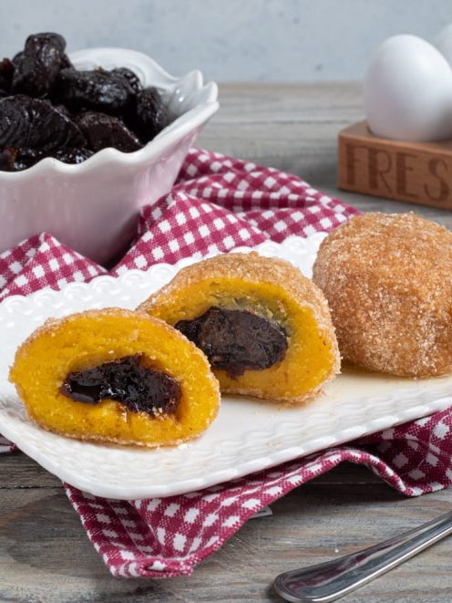 Canederli dolci alle prugne impanati e fritti, uno tagliato a metà rivela il ripieno di prugna