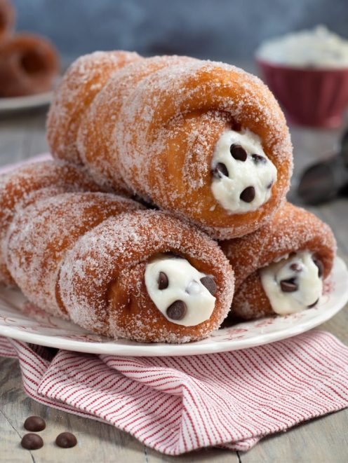 Cartocci siciliani fritti ricoperti di zucchero, farciti con crema di ricotta e gocce di cioccolato