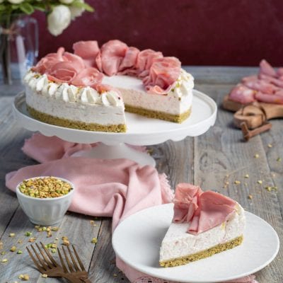 Cheesecake salata con roselline di mortadella, base al pistacchio e una fetta servita sul piatto