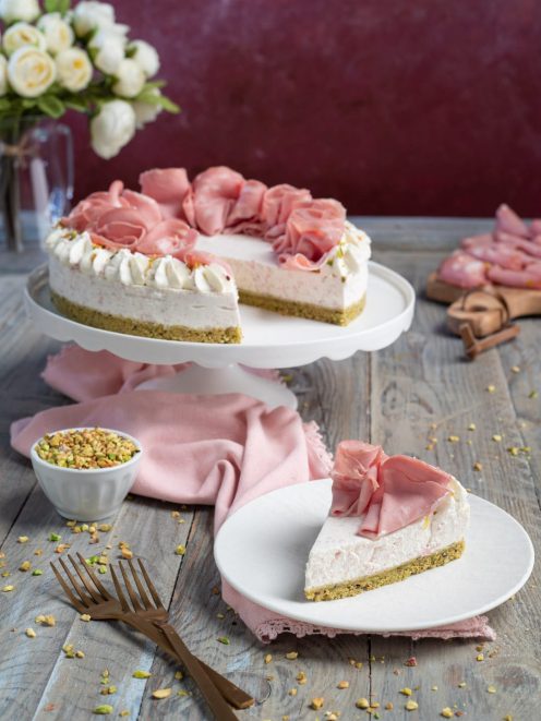 Cheesecake salata con roselline di mortadella, base al pistacchio e una fetta servita sul piatto