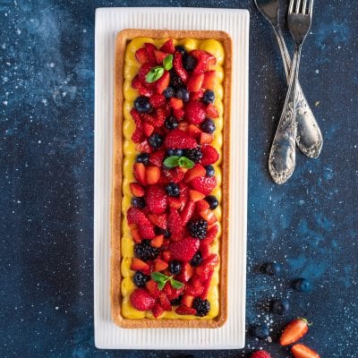 Crostata ai frutti di bosco con crema pasticcera, fragole, mirtilli e more, guarnita con foglie di menta
