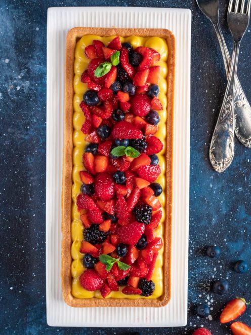 Crostata ai frutti di bosco con crema pasticcera, fragole, mirtilli e more, guarnita con foglie di menta