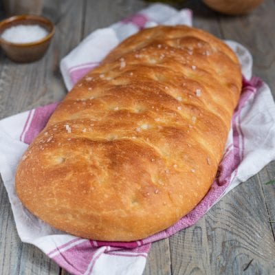 Pan focaccia dalla crosta dorata e croccante, cosparso di fiocchi di sale grosso