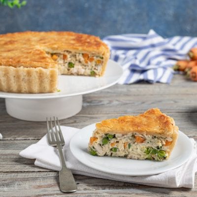 Pasticcio di pollo con crosta dorata, una fetta in primo piano rivela il ripieno con piselli e carote