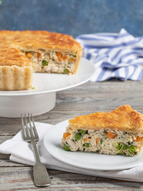 Pasticcio di pollo con crosta dorata, una fetta in primo piano rivela il ripieno con piselli e carote