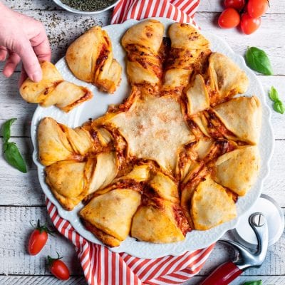 Pizza stella con salsa di pomodoro, servita a spicchi staccabili mentre una mano ne prende uno
