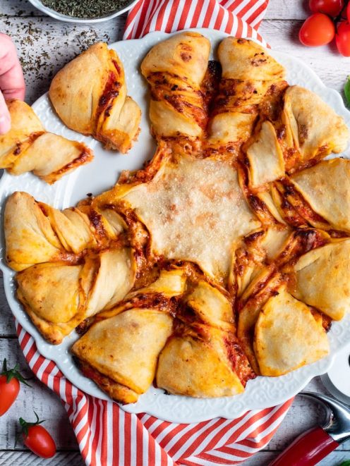 Pizza stella con salsa di pomodoro, servita a spicchi staccabili mentre una mano ne prende uno