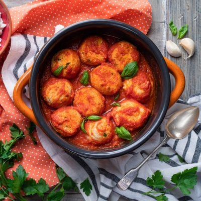 Polpette di ricotta al sugo immerse in salsa di pomodoro e guarnite con foglie di basilico fresco