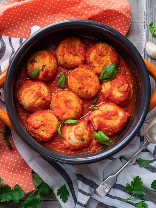Polpette di ricotta al sugo immerse in salsa di pomodoro e guarnite con foglie di basilico fresco