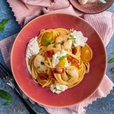 Spaghetti alla chitarra con gamberi, burrata, pomodorini gialli e pancetta croccante guarniti con basilico