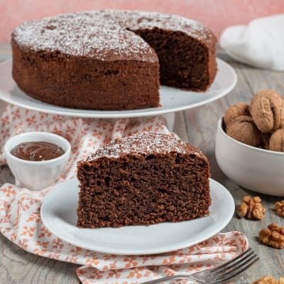 Torta noci e gianduia spolverata di zucchero a velo, con una fetta tagliata che mostra l'interno soffice