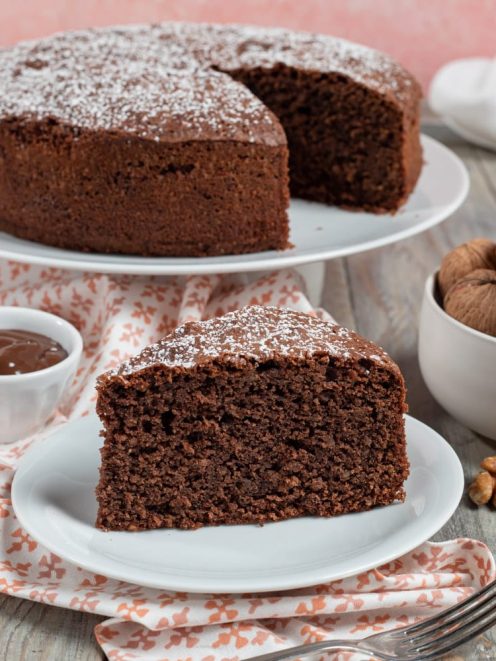Torta noci e gianduia spolverata di zucchero a velo, con una fetta tagliata che mostra l'interno soffice