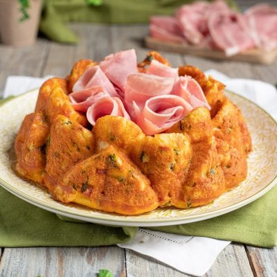 Ciambella salata con prosciutto cotto e zucchine, dorata e soffice, con fette di prosciutto arrotolate al centro