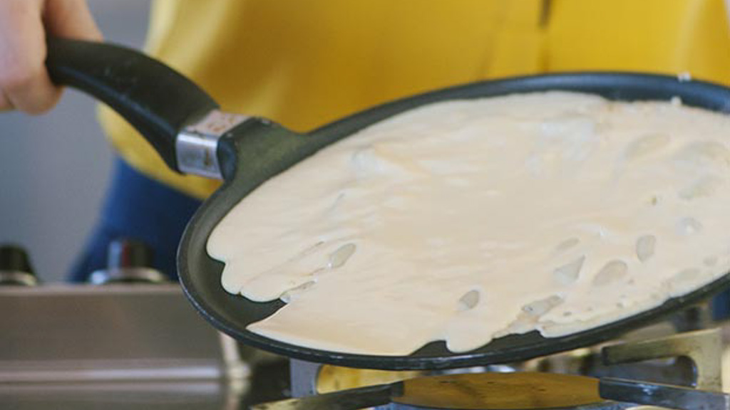 Pastella per crepe distribuita uniformemente sulla padella calda con movimento rotatorio