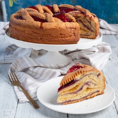 Crostata a strati bicolore con farcia di crema e marmellata, una fetta in primo piano che mostra l'interno