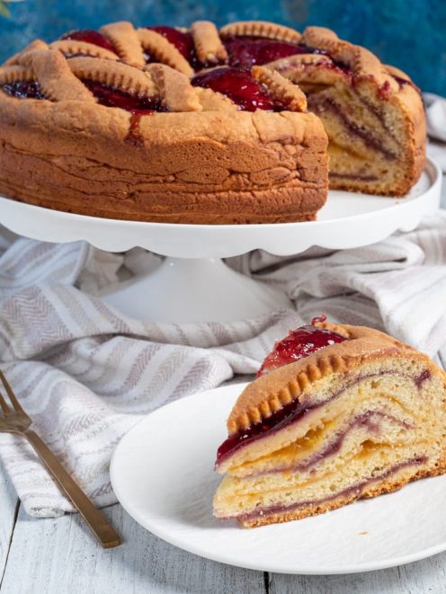 Crostata a strati bicolore con farcia di crema e marmellata, una fetta in primo piano che mostra l'interno