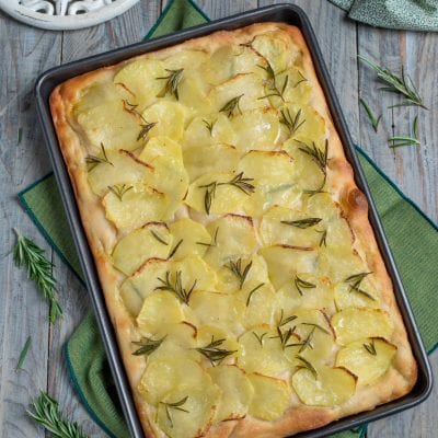 Focaccia con le patate appena sfornata, coperta di fette sottili dorate e rametti di rosmarino