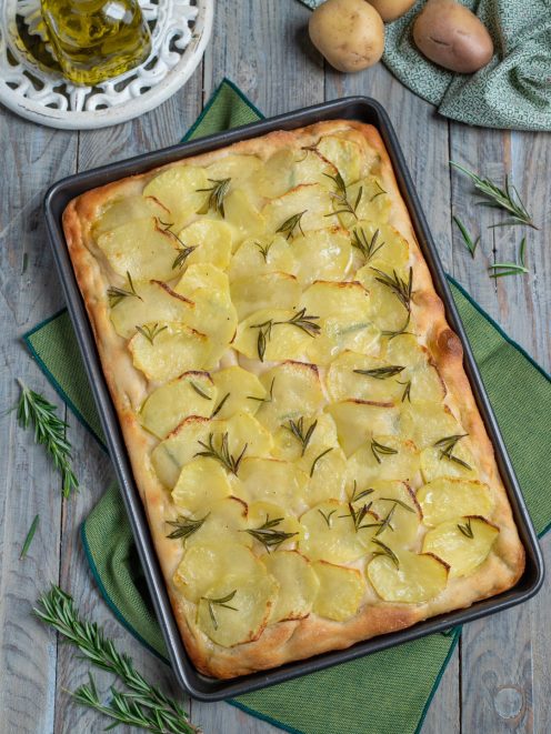 Focaccia con le patate appena sfornata, coperta di fette sottili dorate e rametti di rosmarino