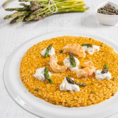 Risotto con scampi, burrata e asparagi selvatici su fondo dorato e cremoso