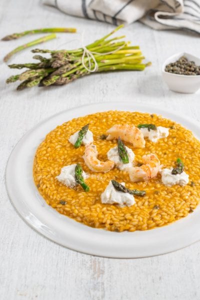 Risotto con scampi, burrata e asparagi selvatici su fondo dorato e cremoso