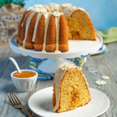 Ciambella alle pesche con glassa e farciture di confettura, decorata con fiorellini di zucchero