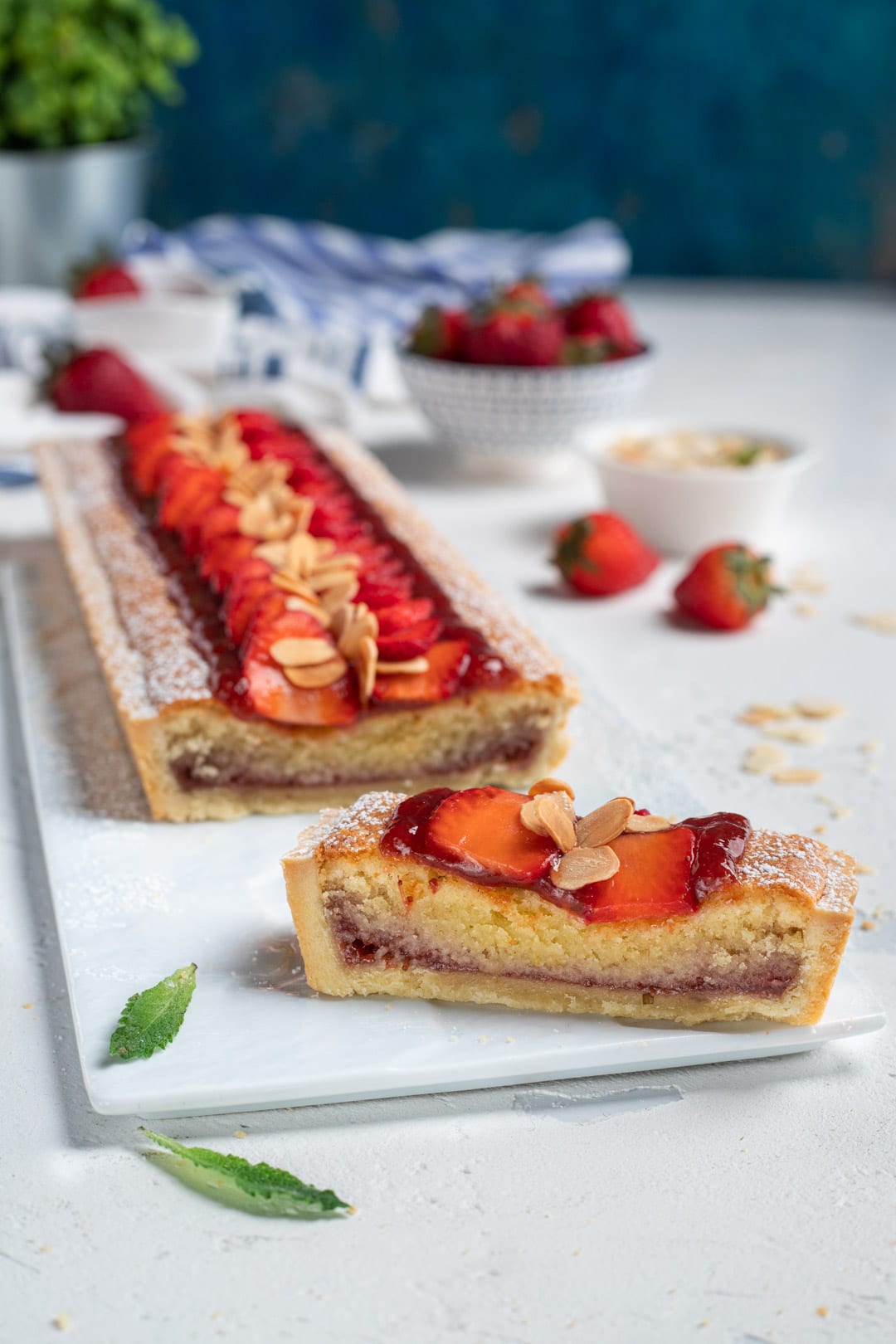 Fetta di crostata frangipane con confettura, fragole fresche a fette e lamelle di mandorle tostate