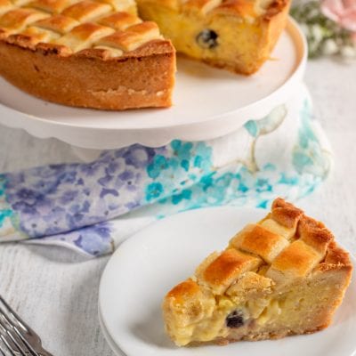 Crostata di riso con reticolo di pasta frolla dorata e ripieno cremoso con gocce di cioccolato, servita a fette
