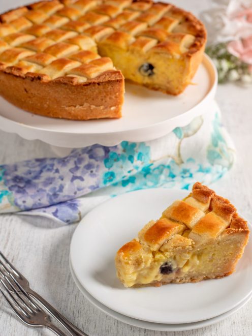 Crostata di riso con reticolo di pasta frolla dorata e ripieno cremoso con gocce di cioccolato, servita a fette
