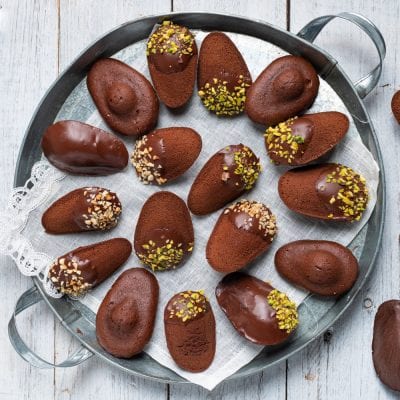 Madeleine al cioccolato glassate, alcune guarnite con granella di pistacchi e nocciole tritate