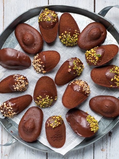 Madeleine al cioccolato glassate, alcune guarnite con granella di pistacchi e nocciole tritate