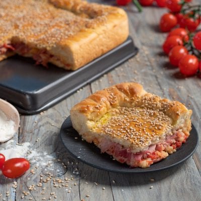 Mattonella palermitana in primo piano con farcitura di pomodoro e salumi, superficie cosparsa di semi di sesamo