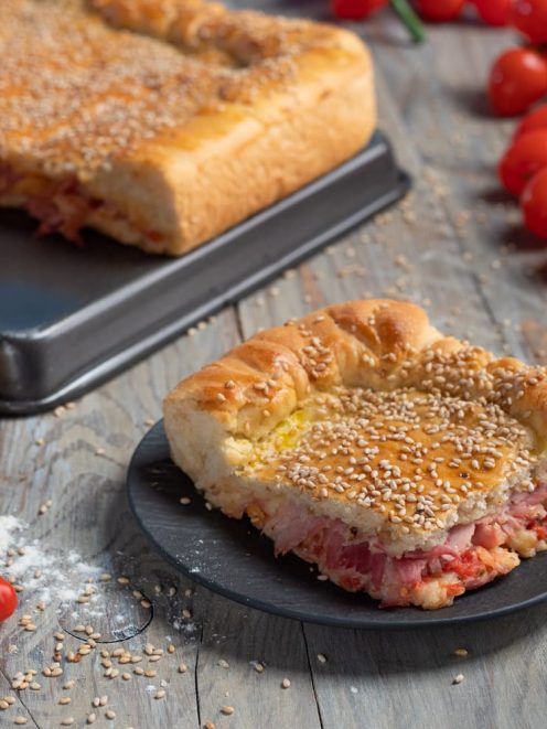 Mattonella palermitana in primo piano con farcitura di pomodoro e salumi, superficie cosparsa di semi di sesamo
