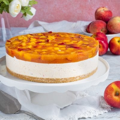 Torta fredda alle pesche con strato di crema, base di biscotto e gelatina di pesche a pezzi in superficie