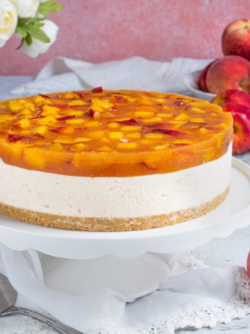 Torta fredda alle pesche con strato di crema, base di biscotto e gelatina di pesche a pezzi in superficie