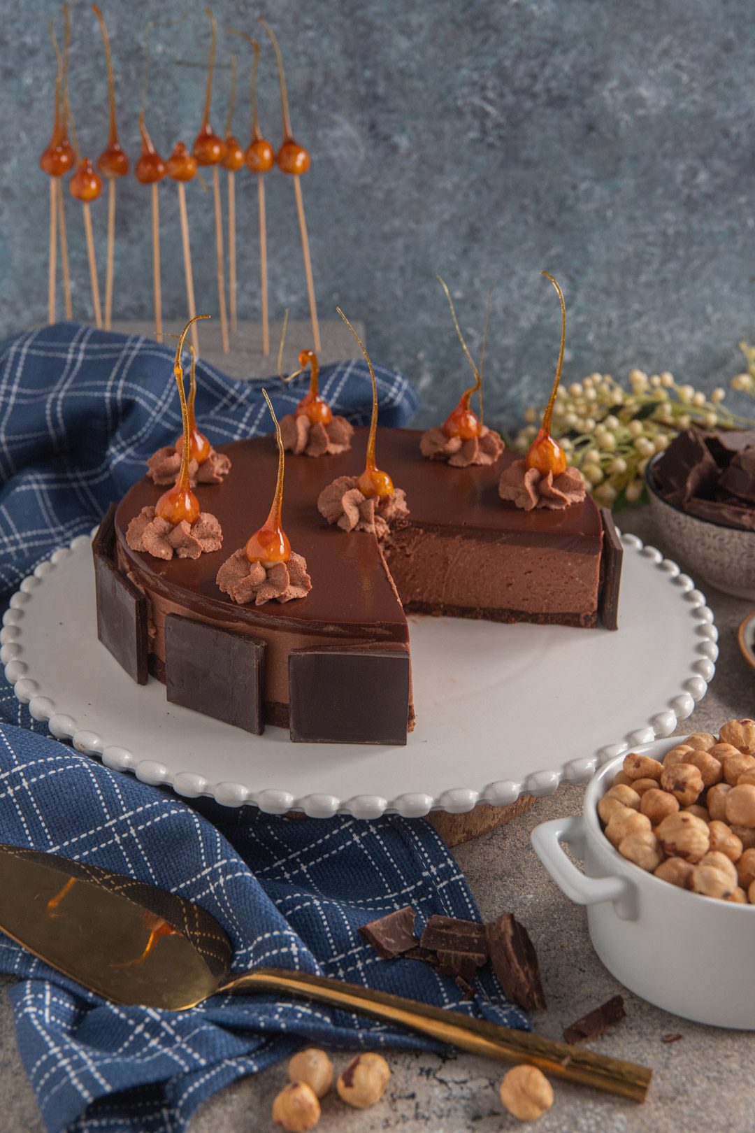 Cheesecake al cioccolato decorata con nocciole caramellate, ciuffi di mousse e pannelli di cioccolato fondente