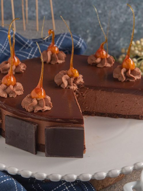 Cheesecake al cioccolato con glassa lucida, pannelli di cioccolato fondente e decorazioni di caramello soffiato