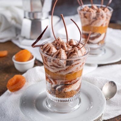 Tiramisù al gianduia e albicocca in coppa con strati di crema, albicocche e riccioli di cioccolato