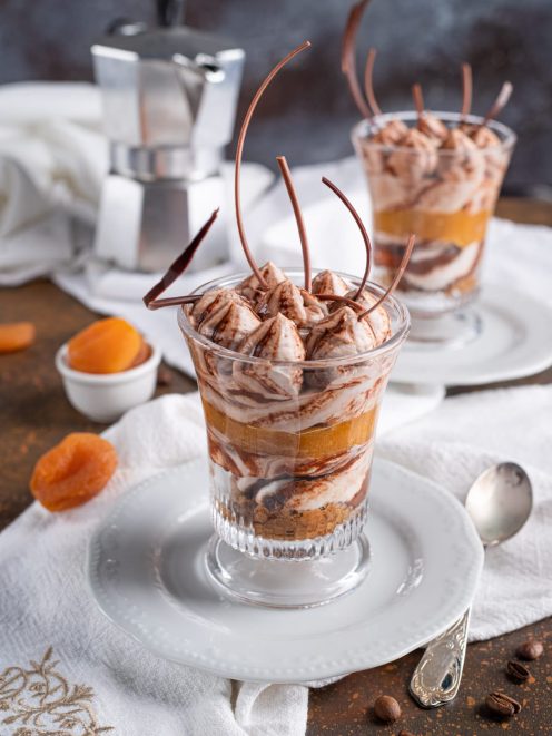 Tiramisù al gianduia e albicocca in coppa con strati di crema, albicocche e riccioli di cioccolato