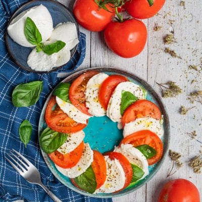 Insalata Caprese con fette di pomodoro e mozzarella alternate, foglie di basilico e origano