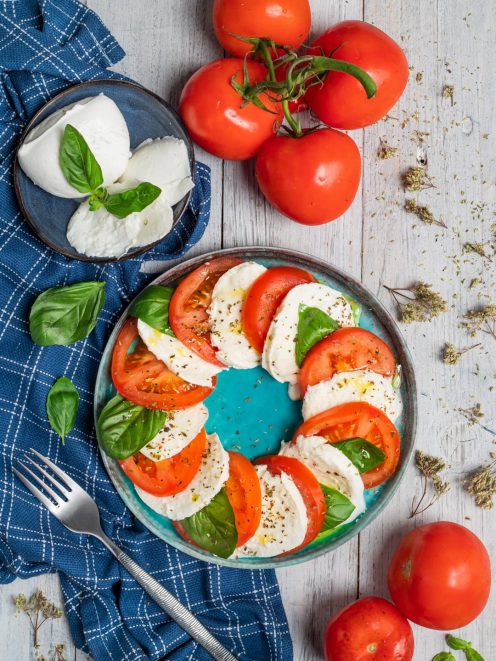 Insalata Caprese con fette di pomodoro e mozzarella alternate, foglie di basilico e origano