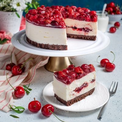 Cheesecake alle ciliegie con base al cioccolato, crema bianca e topping di ciliegie sciroppate, servita a fetta