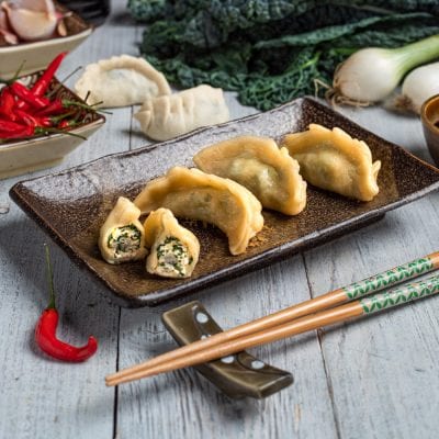 Gyoza dorati serviti interi e tagliati a metà, con ripieno di verdure e carne ben visibile