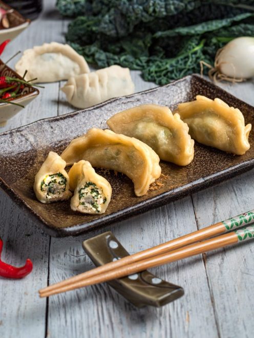 Gyoza dorati serviti interi e tagliati a metà, con ripieno di verdure e carne ben visibile