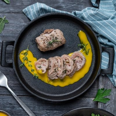 Involtini di vitello affettati con salsa dorata e timo fresco in padella di ferro